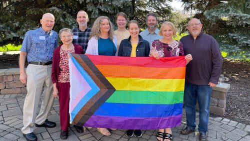 9 people stand with Pride flag in the memorial Garden