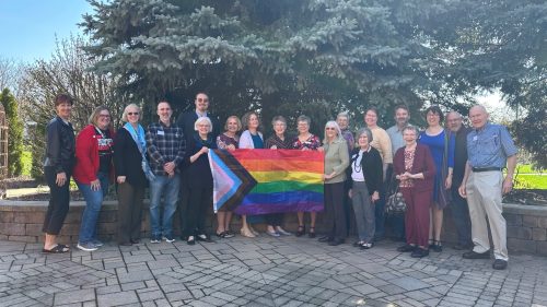 19 people representing Church & Society in memorial garden with pride flag